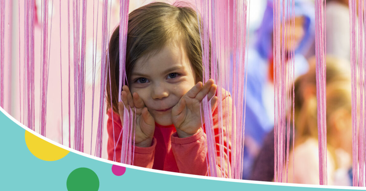 Kuvassa lapsi kurkkaa verhojen takaa